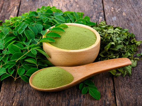 Moringa leaf powder with fresh moringa leaves on rustic wooden surface